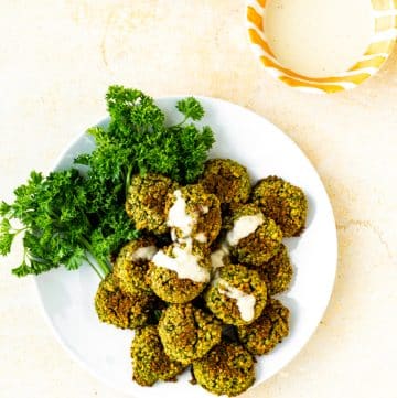 Baked Falafel on top of parsley on white plate drizzled with lemon tahini dressing