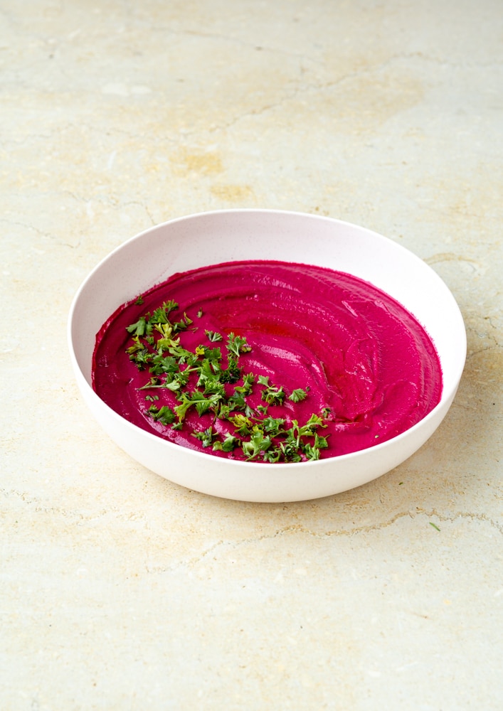 roasted beet hummus with chopped parsley and drizzled olive oil in bowl